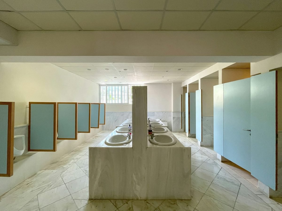 A commercial washroom with a row of sinks and cubicles